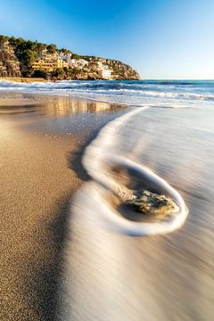 Strand in Mallorca zum Sonnenuntergang mit Wellen die auf den Strand rollen