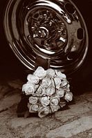 An Elegant White Rose Bouquet Next to a Shiny Chrome Rim on a Stone Pavement in Sepia