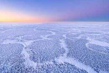 Schöne Strukturen auf einem eisbedeckten IJsselmeer im Winter. Am Horizont geht die Sonne langsam au