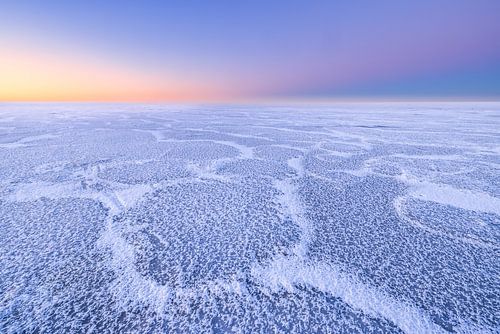 De belles structures sur un IJsselmeer recouvert de glace pendant l'hiver. À l'horizon, le soleil se