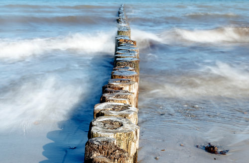 hölzerne Buhnen als Küstenschutz im Meer an einem sonnigen Tag, glattes Wasser bei langer Belichtung