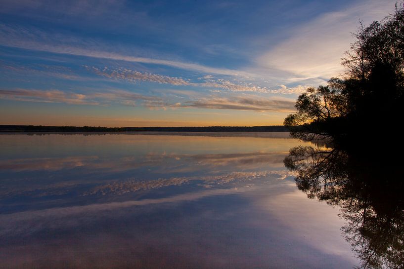 Dawn over the quiet water surface of the lake. The morning blue sky is lit by the orange light of th by Michael Semenov