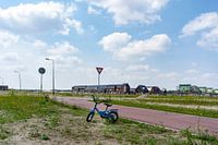 Een kinderfiets staat alleen aan de straat. De nieuwe wijk is in aanbouw.
