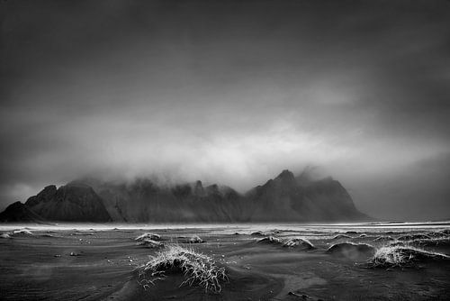 Zwart lavastrand met bergachtergrond op IJsland. Zwart-wit beeld.