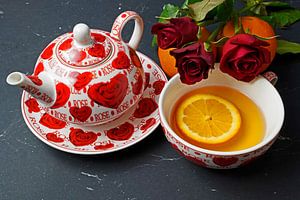 Schwarzer Tee serviert mit Orangenscheibe und roten Rosen