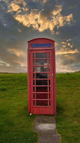 Rode telefooncel in een weiland bij zonsondergang