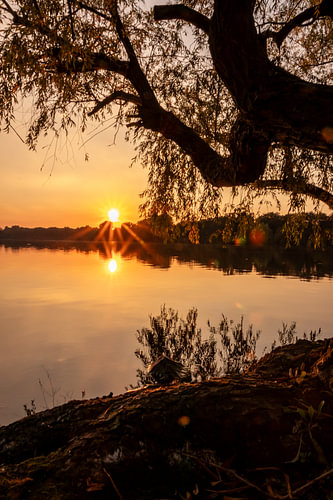 Romantische zonsondergang aan een idyllisch meer met zonneschijn en een schilderachtige weide
