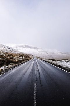 Eine Straße führt durch eine verschneite Landschaft auf den Färöer Inseln
