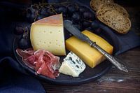 supper plate with various cheese, air dried ham, blue grapes and bread on dark rustic wood, selected