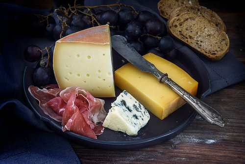 Speiseteller mit verschiedenen Käsesorten, luftgetrocknetem Schinken, blauen Trauben und Brot auf du