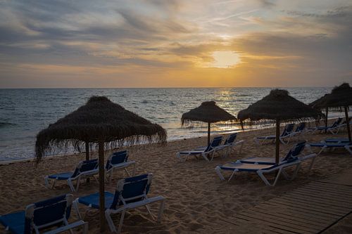 Zonsondergang op het strand met ligbedden en parasols