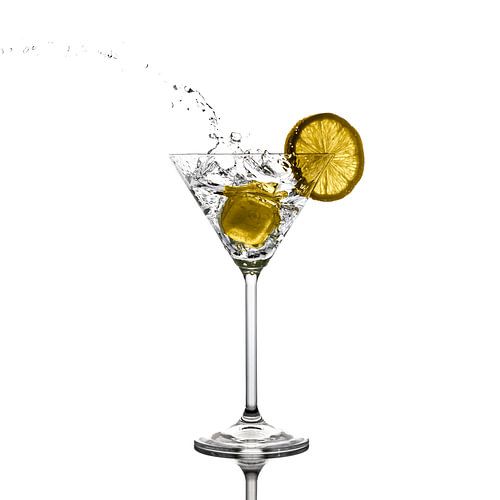 Cheers. Opspattende vloeistof uit een martiniglas door een ingegooid ijsklontje .