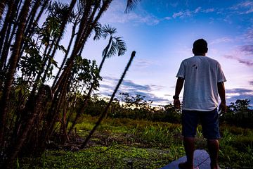 Traditionele man op een kano bij zonsondergang in de Amazone, Peru van John Ozguc