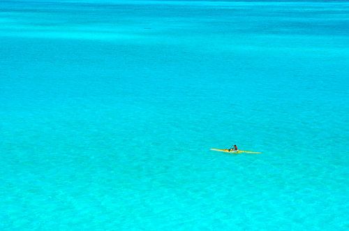 Man in een gele outrigger kano in de blauwe lagune van Bora Bora