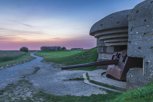 Duitse kustverdedigingsbunker met geschut tijdens kleurrijke zonsopkomst bij Longues-sur-Mer in Normandië, onderdeel van de Atlantikwall en een indrukwekkend overblijfsel uit de Tweede Wereldoorlog aan de Franse kust.