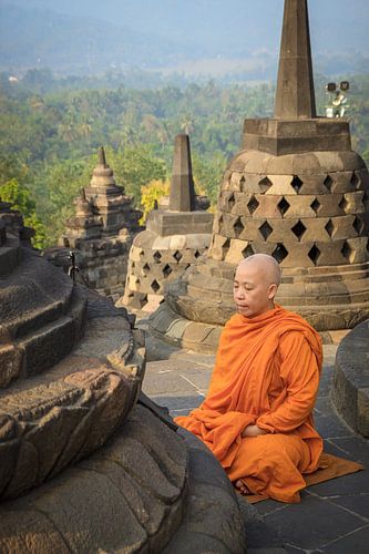 Boeddhistische monnik in oranje gewaad mediteert op de Borobudur bij zonsopkomst
