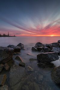 Beau ciel rouge matinal sur l'IJsselmeer près de Den Oever. Les pierres et les poteaux au premier plan, ainsi que le phare à l'horizon marquant l'entrée du port, créent un bel effet de profondeur. La vitesse d'obturation longue apporte du calme à la photo. Un beau moment de plaisir sur les eaux hollandaises.