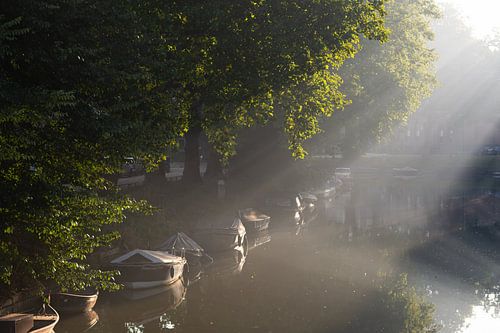 The sun breaks through and shines on the boats in the canals of Utrecht
