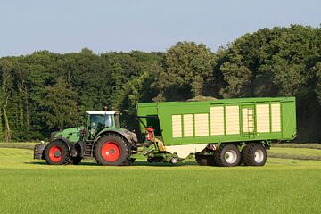 Groene tractor die gemaaid gras opraapt met een groene opraapwagen in de zomer in Nederland van Tonko Oosterink