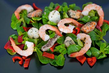 Feldsalat mit Paprika und Meeresfrüchten auf schwarzer Servierplatte angerichtet