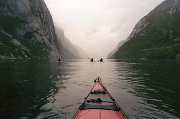 Vue d'un kayak rouge dans le Lysefjord en Norvège au crépuscule à la fin d'une journée nuageuse