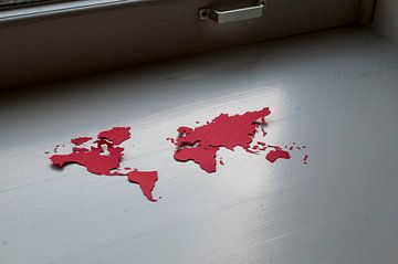 Kwetsbare aarde. Wereldkaart, uitgeknipt in rood papier, in de vensterbank van Irene Cecile