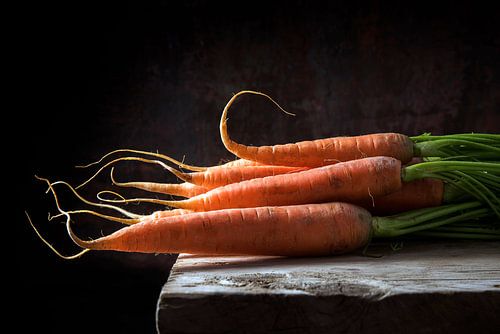 Carrots with green leaves on a rustic wooden table against a dark background with copy space, backli