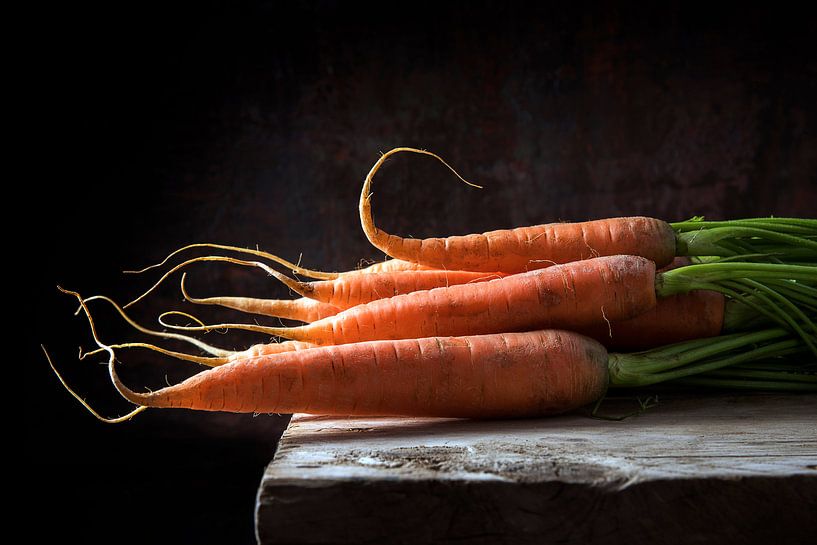 Carrots with green leaves on a rustic wooden table against a dark background with copy space, backli by Maren Winter