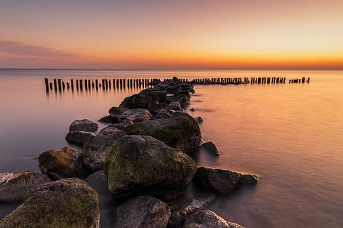 Een waterkering van grote stenen en paaltjes in het IJsselmeer bij een gouden zonsopkomst
