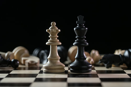 Schachfiguren Königin und König vor einem von gefallenen Schachfiguren nach einem Schlachtfeld auf e
