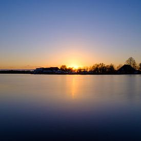 Soleil couchant au bord d'un lac, vue sur des bateaux et des chalets. sur Lidewij Olive