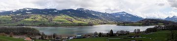 Panoramafoto van een besneeuwd en gedeeltelijk bewolkt berglandschap in Zwitserland met het Gruyèremeer van Andreas Freund