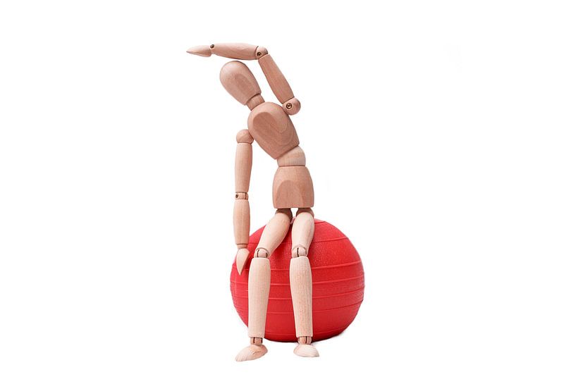 Wooden doll is standing on a red gym ball by Michar Peppenster