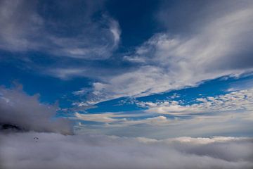 Wit wolkenveld onderaan, boven de blauwe lucht, links een kleine paraglider, vrijheid., Luchtfoto.