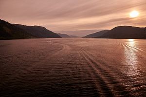 Nordfjord in West-Norwegen mit glattem Wasser und hochaufragenden Gipfeln, an deren Fuß einige Bauernhöfe im Sonnenschein erstrahlen