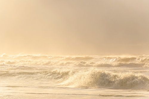 De golven slaan tegen het strand tijdens een stormachtige zonsondergang