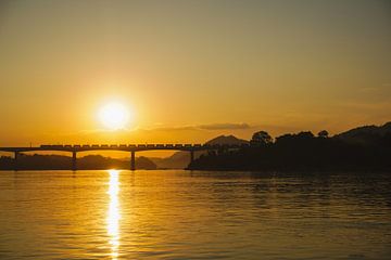 Trein op brug tijdens zonsondergang in Laos van Ilse Tromp