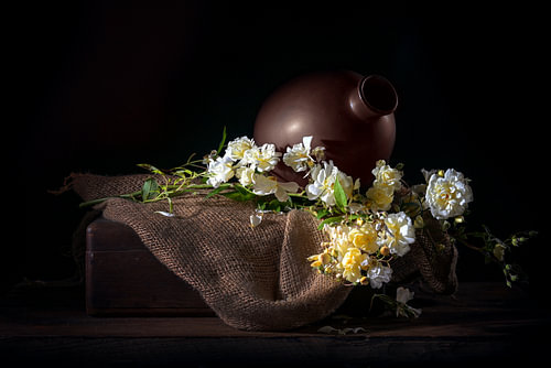 Rosenzweig mit zarten gelben weißen Blüten auf rustikalem Sackleinen,