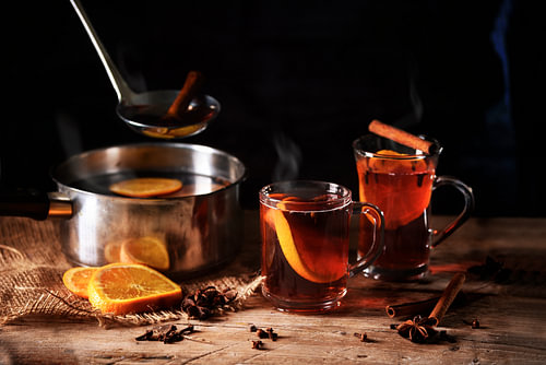 heiß dampfender Glühwein, der in einem Topf gekocht und in Glasbechern mit weihnachtlichen Gewürzen 