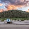 Strandhuisje op het strand bij opkomende zon aan de noorzeekust in Zeeland tegen een roze oranje bew van Wout Kok