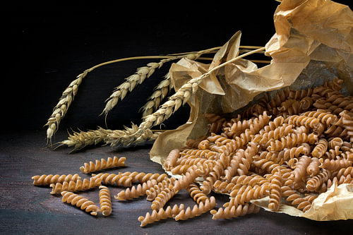 Vollkornnudeln mit Fusilli aus Bio-Dinkel in einer Papiertüte und ein paar Ähren auf dunklem, rustik