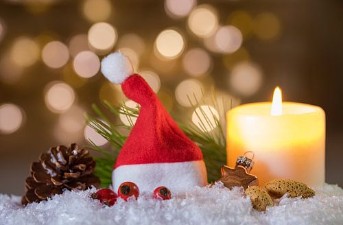 Kerst- of adventsdecoratie met brandende kaars en rode kerstmuts op sneeuw