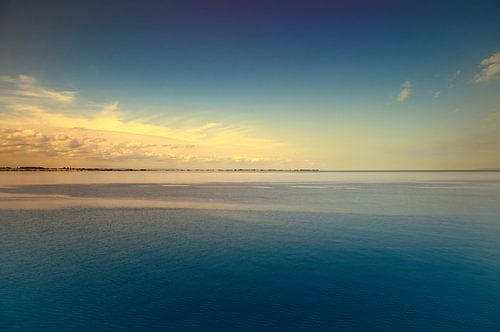 Een rustig zeegezicht onder een heldere hemel. Het water weerspiegelt zachte wolken.