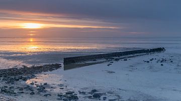Oude golfbreker en stenen liggen droog tijdens eb op de Waddenzee bij zonsondergang van Bram Lubbers