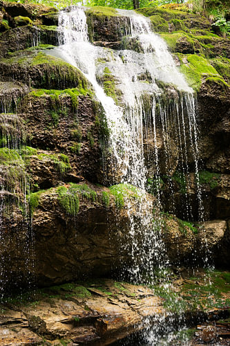 Een waterval stort zich over met mos begroeide rotsen