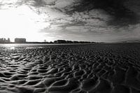 Vaste plage de sable avec silhouette de ville sous un ciel bleu lumineux en noir et blanc.