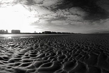 Uitgestrekt Zandstrand Met Stadssilhouet Onder Heldere Blauwe Lucht in zwart-wit.