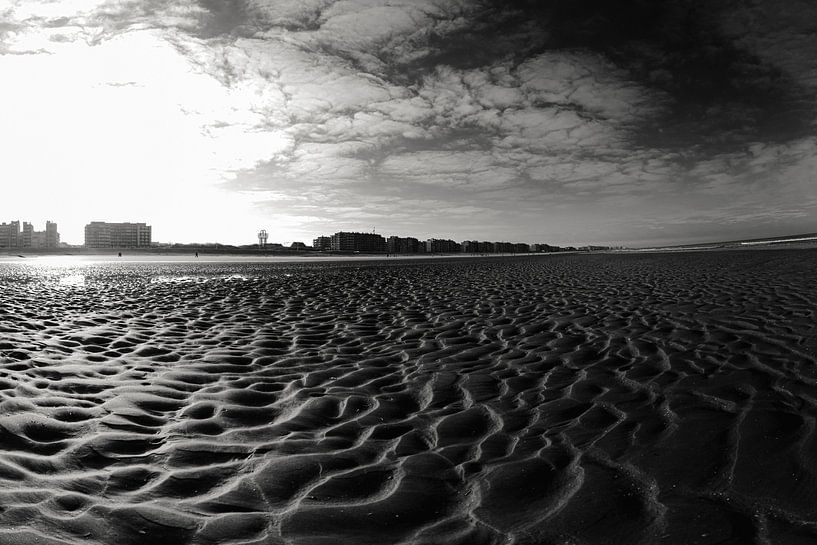 Vast Sandy Beach With City Silhouette Under Bright Blue Sky in black and white. by Youri Mahieu