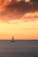 Segelboot gegen einen orangefarbenen bewölkten Himmel