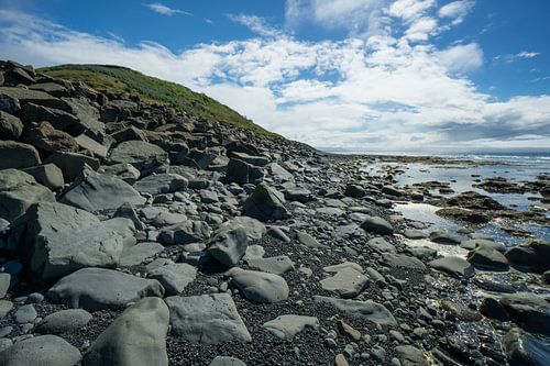 Islande - Colline verte derrière un rivage pierreux et eau réfléchissante